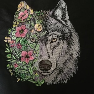 Peut inclure: Broderie représentant un visage de loup entouré de fleurs roses, jaunes et vertes.