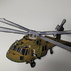 Pode incluir: Um remendo bordado de um helicóptero militar, com cores verde e preta e pás brancas.