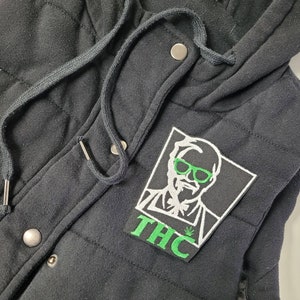 May include: Black hooded jacket with a green and white patch featuring a cartoon character wearing sunglasses and the word "THC".