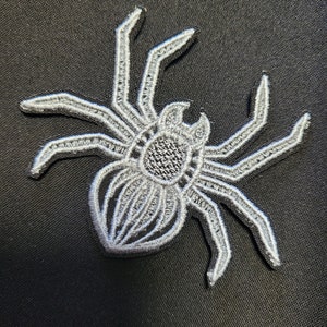 May include: A white embroidered spider patch with detailed legs and a textured body.