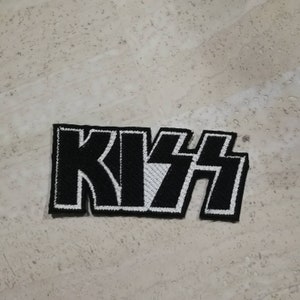 May include: Black and white embroidered KISS logo patch. The patch is made of fabric and has a white outline.