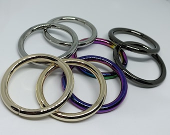 Puede incluir: Un conjunto de ocho anillos metálicos de varios colores, incluyendo oro, plata, negro e iridiscente. Los anillos son todos aproximadamente del mismo tamaño y están dispuestos en una pila.
