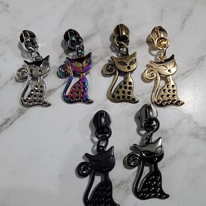 May include: Assortment of six zipper pulls featuring a cat design. The zipper pulls are made of metal and come in a variety of colours, including silver, gold, black, and iridescent.