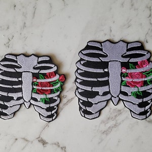 May include: Two embroidered patches featuring a ribcage with a cluster of red roses in the centre. The larger patch is approximately 7 inches wide and the smaller patch is approximately 4 inches wide.