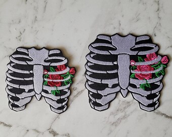 May include: Two embroidered patches featuring a ribcage with a cluster of red roses in the center. The larger patch is approximately 7 inches wide and the smaller patch is approximately 4 inches wide.