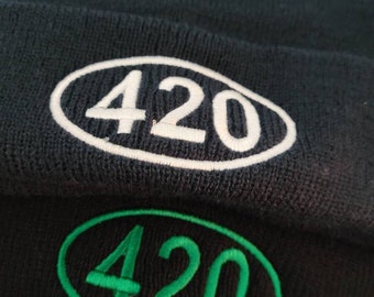 Puede incluir: Dos gorros de punto negros. Uno tiene un óvalo bordado blanco con el número "420". El otro tiene un óvalo bordado verde con el número "420".