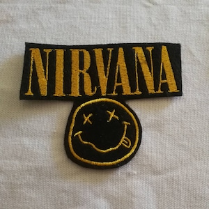May include: Black and yellow embroidered patch with the word "NIRVANA" and a smiley face with an X for eyes.