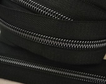 Puede incluir: Primer plano de una cinta de cremallera negra con dientes de cremallera de metal plateado. La cinta de cremallera está doblada en capas.