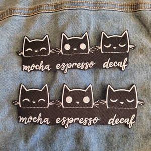 May include: Two rows of black cat patches with white embroidery. The top row reads "mocha espresso decaf" and the bottom row reads "mocha espresso decaf".