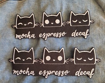 Puede incluir: Dos filas de parches de gatos negros con bordados blancos. La fila superior dice "mocha espresso decaf" y la fila inferior dice "mocha espresso decaf".