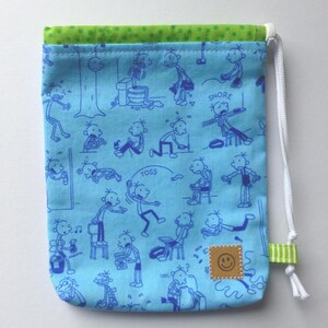 Könnte beinhalten: Ein hellblaues Kordelzugbeutel mit grünem Oberteil und weißem Kordelzug. Die Tasche zeigt eine sich wiederholende blaue Cartoon-Illustration. Ein kleines quadratisches Patch mit einem lächelnden Gesicht befindet sich auf der unteren rechten Seite.