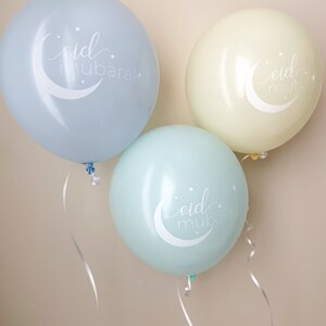 May include: Three balloons with the phrase "eid mubarak" written on them. The balloons are light blue, light green, and yellow.
