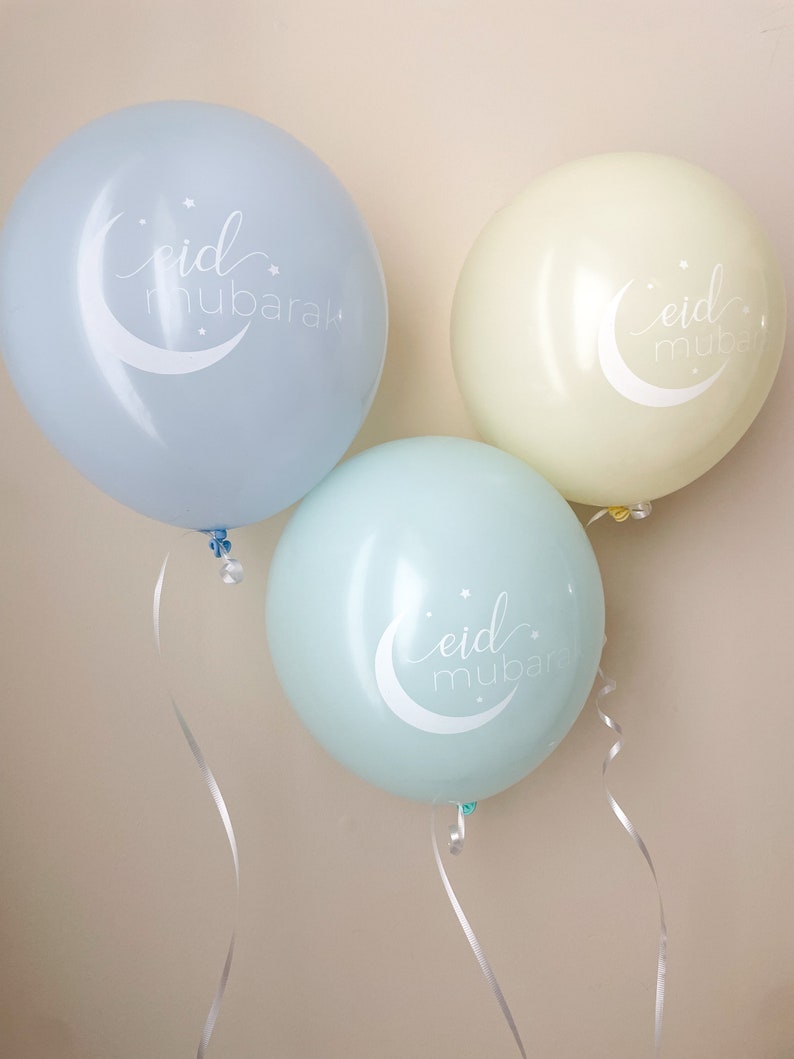 May include: Three balloons with the phrase "eid mubarak" written on them. The balloons are light blue, light green, and yellow.