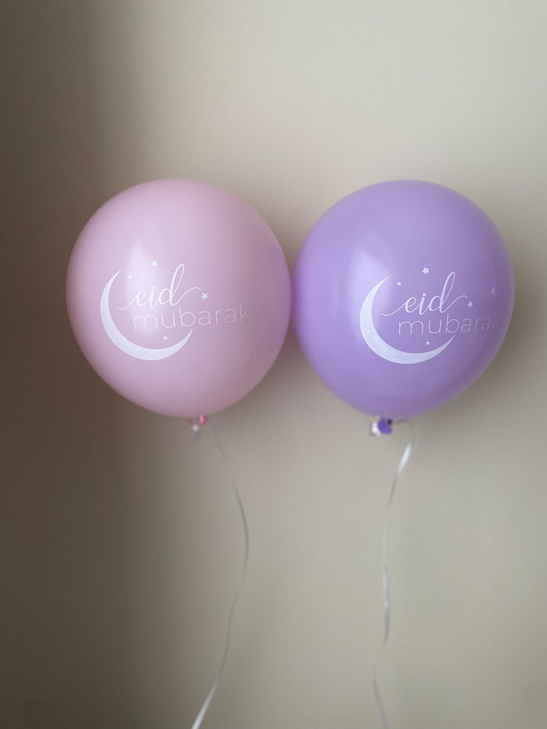 May include: Two balloons, one pink and one purple, with the text "eid mubarak" in white lettering. The balloons are tied with white strings.