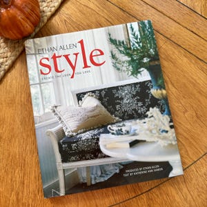 May include: A hardcover book titled Ethan Allen style create the look you love, produced by Ethan Allen with text by Katherine Ann Samon. The cover features a photograph of a black and white patterned settee with a beige tasseled pillow.