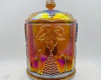 May include: A vintage iridescent glass candy jar with a grapevine design. The jar is a deep amber color with purple and blue iridescent highlights. The lid features a grape cluster finial.