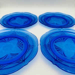Könnte beinhalten: Vier kobaltblaue Dessertteller aus Glas mit einem dekorativen, geätzten Design. Die Teller haben einen gewellten Rand.