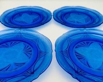 May include: Four cobalt blue glass dessert plates with a decorative etched design. The plates have a scalloped edge.