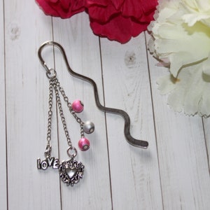 May include: Silver bookmark with a heart charm and the word "love" hanging from three chains with pink and silver beads.