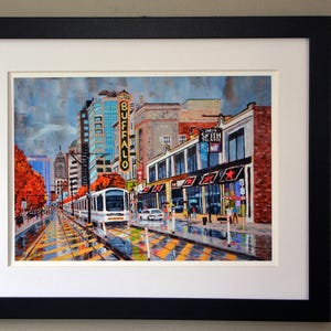 May include: A painting of a city street scene with a streetcar in the foreground. The streetcar is white with red and blue accents. The buildings in the background are brick and have signs that say "Buffalo" and "Shea's Smith Music Hall".