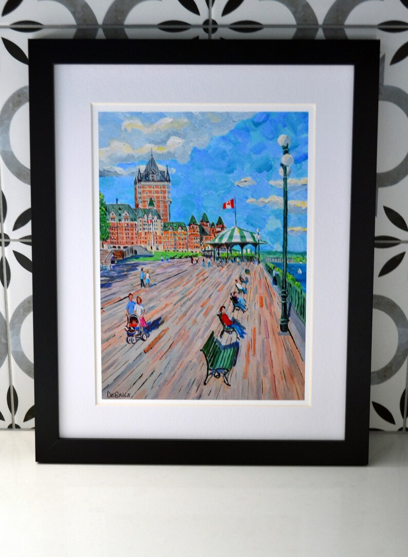 May include: A framed painting of a waterfront scene with a large building in the background. The painting is done in a colorful, impressionistic style. The building is a light brown color with white trim and a green roof. There are people walking on the boardwalk in front of the building. The sky is blue with white clouds. The painting is signed "DeBaets" in the lower left corner.