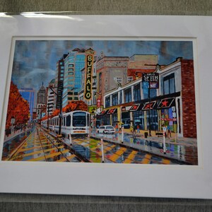 May include: A painting of a city street scene with a streetcar in the foreground. The streetcar is white with a red stripe and is traveling down a street lined with buildings. The buildings are brick and have storefronts. There are trees on either side of the street and people walking on the sidewalk. The sky is cloudy and there is a sign that says "Buffalo" on one of the buildings.