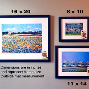 May include: Three framed paintings with different scenes. The top left painting is a landscape with a field of sunflowers, the top right painting shows a row of colorful beach houses, and the bottom right painting shows a row of white beach houses. The dimensions of the frames are listed below each painting.