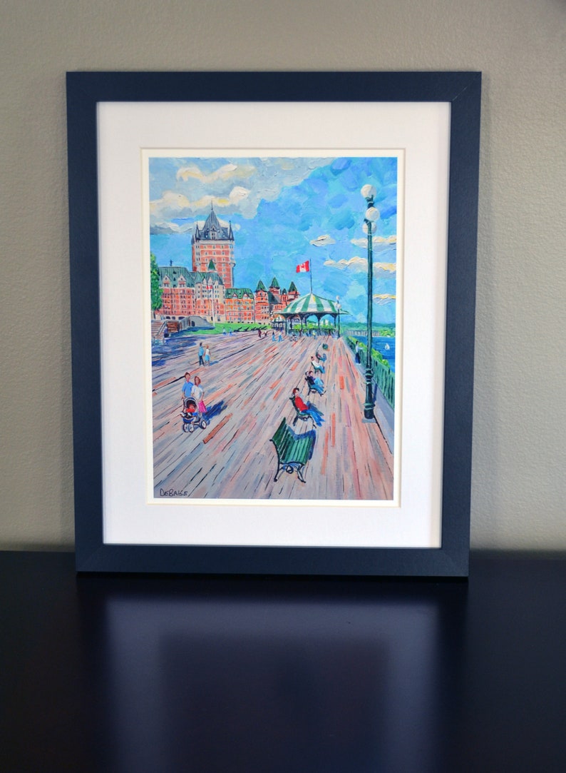 May include: A framed painting of a waterfront scene with a large building in the background. The painting is done in a colorful, impressionistic style. The building is red and white and has a green roof. There are people walking on the boardwalk in front of the building. The sky is blue with white clouds. The painting is signed "DeBaise" in the lower left corner.