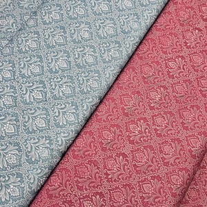 Peut inclure: Deux échantillons de tissu avec un motif floral répétitif. L'un est bleu poussiéreux et l'autre rouge profond. Le motif présente des fleurs et des feuilles stylisées dans un design symétrique, avec un contour blanc. Le tissu est probablement en coton ou en lin.