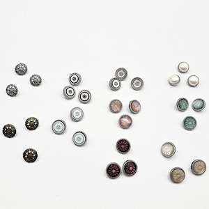 Peut inclure: Une collection de boutons décoratifs aux motifs et couleurs variés. Les boutons comprennent des filigranes métalliques ornés, des motifs noir et blanc, des motifs floraux et des accents nacrés. Les boutons sont disposés sur une surface blanche.