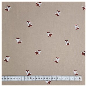 Pu&ograve; includere: Tessuto beige con un motivo ripetitivo di volpi marroni. Il tessuto &egrave; misurato con un righello in centimetri.