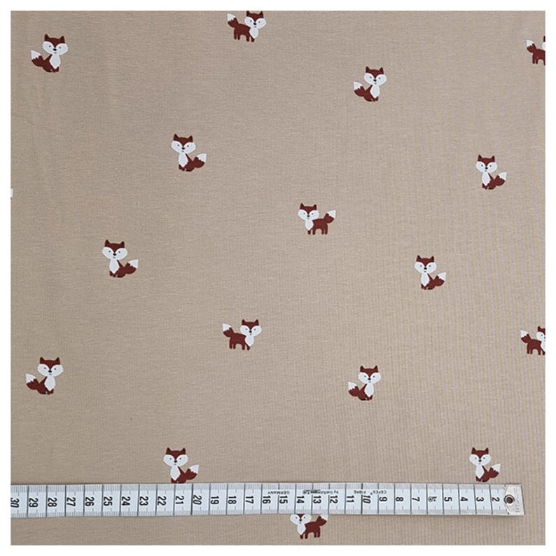 Pu&ograve; includere: Tessuto beige con un motivo ripetitivo di volpi marroni. Il tessuto &egrave; misurato con un righello in centimetri.