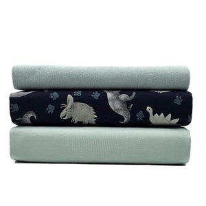 Könnte beinhalten: Drei Stoffmuster, die übereinander gestapelt sind. Die oberen und unteren Muster sind hellblau. Das mittlere Muster ist dunkelblau mit einem Muster aus Dinosauriern und Fußabdrücken.