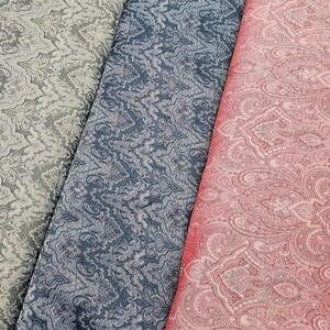 Könnte beinhalten: Nahaufnahme von drei Stoffmustern mit verzierten Paisley-Mustern. Die Muster sind in Grau-, Blau- und Rosatönen gehalten. Der Stoff hat eine strukturierte Optik, wobei das Muster leicht vom Hintergrund abgehoben ist.