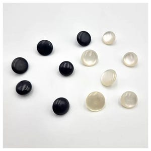 Può includere: Assortimento di bottoni rotondi in nero e bianco. I bottoni sono lisci e hanno una finitura lucida.