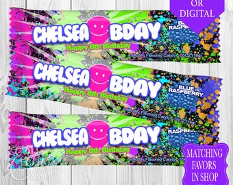 Pode incluir: Um embrulho de barra de chocolate colorido com um design de pintura salpicada. O embrulho diz "Chelsea Bday Happy 8th Birthday" e apresenta uma barra de chocolate de framboesa azul.