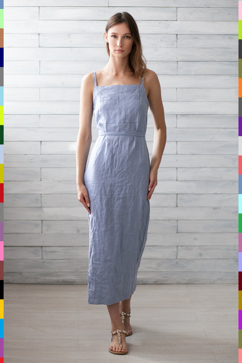 May include: A light blue linen dress with thin straps and a tie belt. The dress is midi length and has a relaxed fit.
