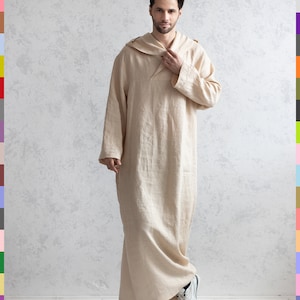 May include: A person wearing a long, beige linen robe with a hood. The robe has a simple design and is loose-fitting. The person is standing on a light-colored floor in front of a textured wall.