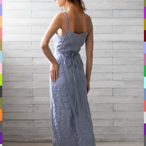 May include: A light blue linen wrap dress with thin straps and a tie at the waist. The dress is midi length and has a relaxed fit.