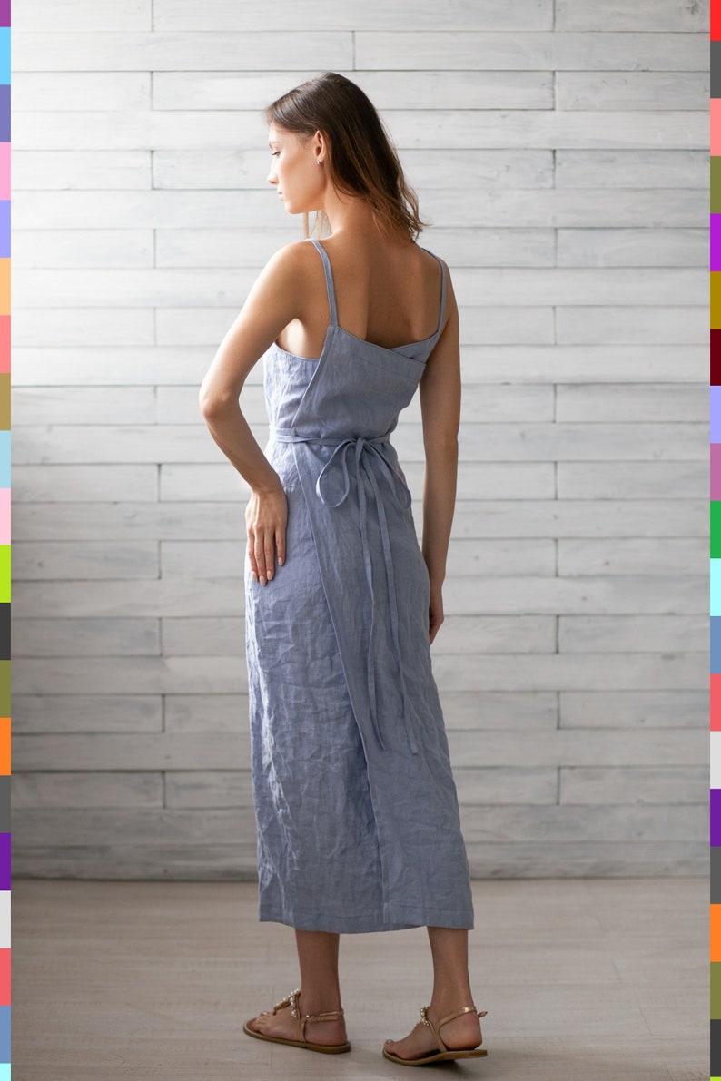 May include: A light blue linen wrap dress with thin straps and a tie at the waist. The dress is midi length and has a relaxed fit.