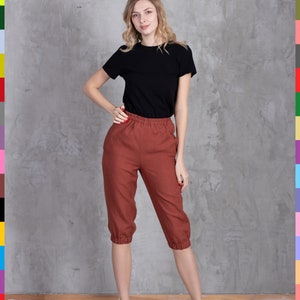 Może przedstawiać: Osoba w czarnym t-shircie i spodniach capri w kolorze rdzy. Spodnie capri mają elastyczną talię i marszczone mankiety. Osoba ma również na sobie czarne sandały. Tło to szara betonowa ściana.