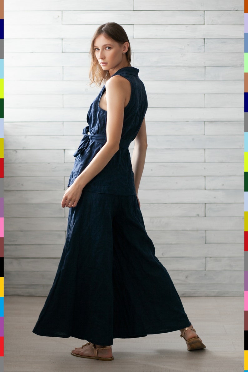 K&ouml;nnte beinhalten: Ein marineblaues &auml;rmelloses Oberteil und eine Hose mit weitem Bein. Das Oberteil hat eine Schleife an der Taille und einen Kragen. Die Hose ist bodenlang. Das Outfit ist aus einem strukturierten Stoff gefertigt. Das Model tr&auml;gt hellbraune Sandalen.
