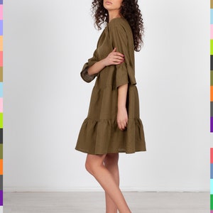 May include: A woman wearing a brown linen dress with a tiered skirt. The dress has a relaxed fit and 3/4 sleeves.