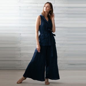 K&ouml;nnte beinhalten: Ein marineblaues zweiteiliges Outfit aus Leinen. Das &auml;rmellose Oberteil hat ein Wickeldesign mit passendem G&uuml;rtel. Die weite Hose vervollst&auml;ndigt das Ensemble. Das Outfit ist aus leichtem, flie&szlig;endem Stoff gefertigt.