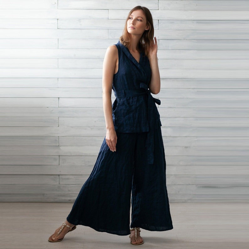 K&ouml;nnte beinhalten: Ein marineblaues zweiteiliges Outfit aus Leinen. Das &auml;rmellose Oberteil hat ein Wickeldesign mit passendem G&uuml;rtel. Die weite Hose vervollst&auml;ndigt das Ensemble. Das Outfit ist aus leichtem, flie&szlig;endem Stoff gefertigt.