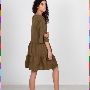 May include: A brown linen dress with a tiered skirt and 3/4 sleeves. The dress is loose-fitting and has a relaxed silhouette.