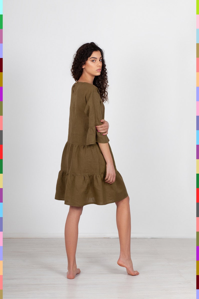 May include: A brown linen dress with a tiered skirt and 3/4 sleeves. The dress is loose-fitting and has a relaxed silhouette.