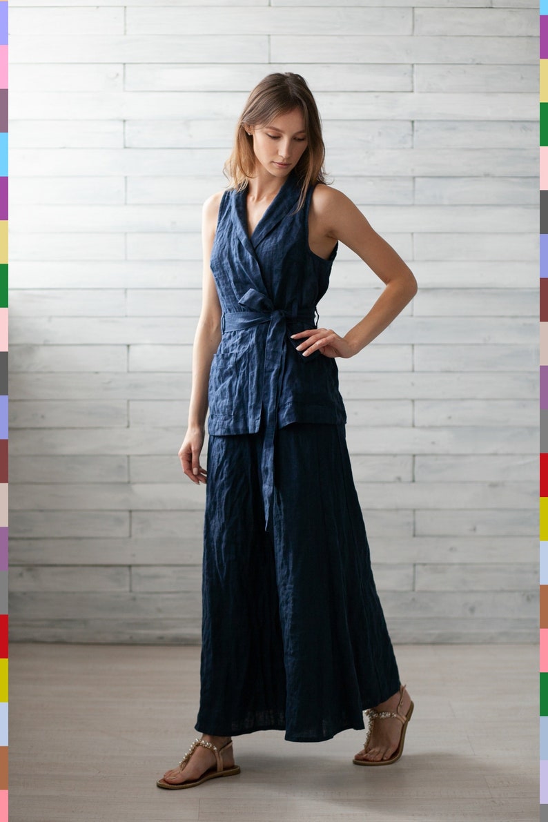 K&ouml;nnte beinhalten: Ein marineblaues Leinen-Ensemble aus Wickel-Top und weitem Hosenbein. Das &auml;rmellose Top hat einen Bindverschluss in der Taille. Das Model tr&auml;gt goldene Sandalen. Das Outfit ist aus einem strukturierten Stoff gefertigt.