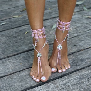 Puede incluir: Sandalias de pies descalzos con cuentas rosas y dijes de árbol de la vida plateados. Las sandalias se atan alrededor de los tobillos y tienen un aspecto delicado y femenino.