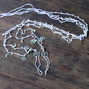 May include: White crocheted necklace with silver tree and crescent moon charms. The necklace is layered and has a delicate, bohemian style.